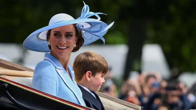 The Princess of Wales smiles as she sits next to her son Prince Louis in a carriage on The Mall