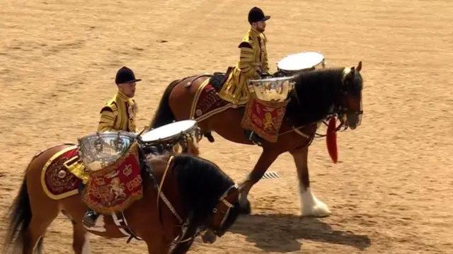 Two guards ride horses while playing the drums