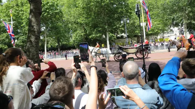 Royal watchers hold their phones up as the King and Queen pass by on The Mall