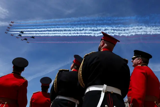 Members of the British military watch the Red Arrows perform a flypast