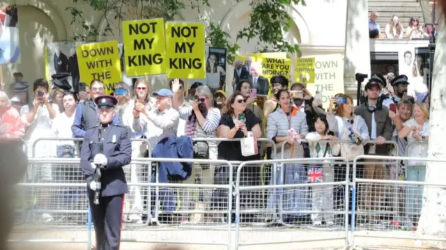 A group of protesters holding up signs saying 'Not My King' and 'Down with the Crown' can be seen in the crowds on The Mall
