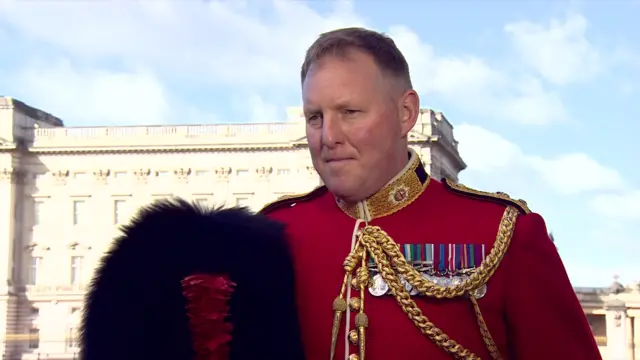 Lieutenant Colonel Charles Foinette stands in front of Buckingham Palace in full military dress holding his black hat