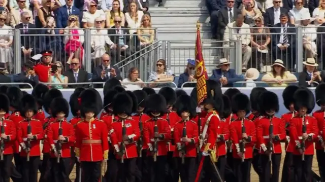 Foot guards of the Grenadier Guards stand as a flag is carried passed them
