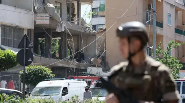A Lebanese soldier in army uniform is pictured holding a rifle in front of a damaged apartment building.