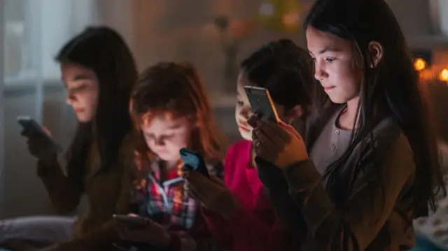 Stock image of a group of children scrolling through social media in a dark room