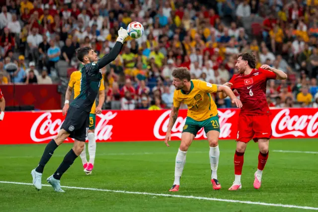 Patrick Beach (L) of Australia makes a save as Cameron Burgess (C) and Orkun Kokcu (R) of Turkey watch during the first half of the FIFA World Cup 2026 group stage match between Australia and Turkey, Vancouver, Canada