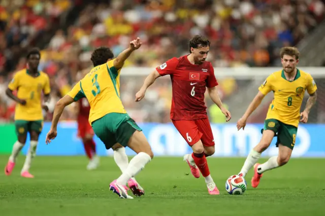 Orkun Kokcu #6 of Turkiye runs with the ball under pressure from Alessandro Circati #3 and Connor Metcalfe #8 of Australia during the FIFA World Cup 2026 Group D match between Australia and Türkiye at BC Place Vancouver