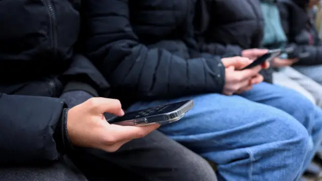 Several children sit in a row on their phones