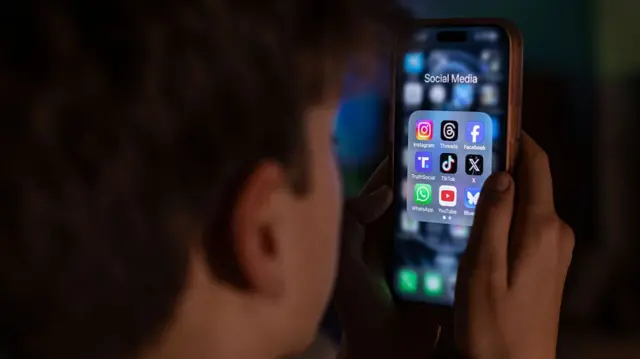 A teenage boy looks at social media apps on his phone