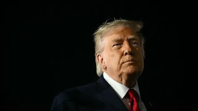 Close up of Donald Trump in black suit and red tie as he looks to the left. Black background