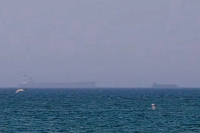 A hazy view of commercial vessels waiting in the Gulf of Oman after applying for transit permits to pass through the Strait of Hormuz