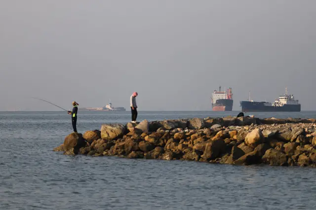 Fisherman off Strait of Hormuz with three large ships in the background