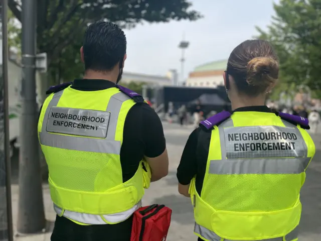 A view of two people fro behind wearing "Neighbourhood Enforcement" branded jackets