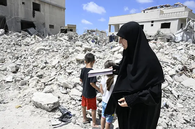 a woman and two children standing in front of a giant pile of rubble