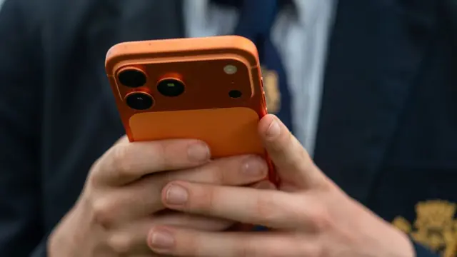 Boy looks at mobile phone with orange case.