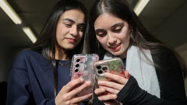 Two young teenage girls use their iphones next to each other