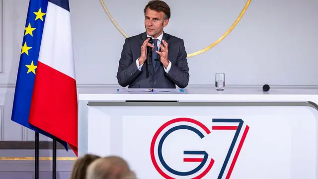 Macron speaking into a microphone behind a white desk with "G7" written on it