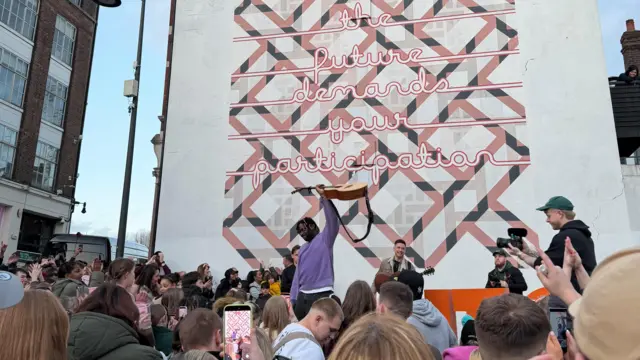 Myles Smith in Luton holding a guitar above his head surrounded by crowds