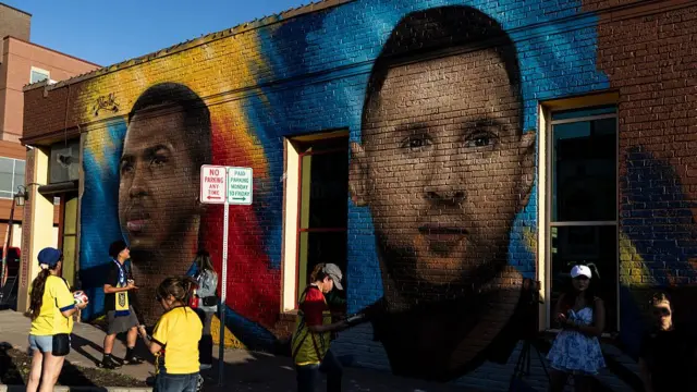 : People stand next to mural titled "Dos Naciones, Una Pasión" (Two Nations, One Passion), with Lionel Messi alongside an Ecuadorian football player painted by LA-based Ecuadorian artist MisterAlek on June 16, 2026 in Kansas City, Missourig