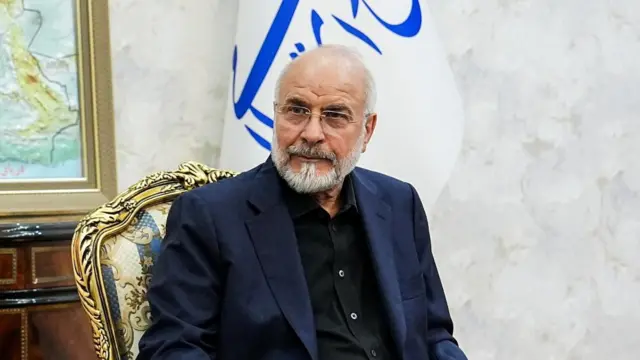 Mohammad Ghalibaf in front of a blue and white flag