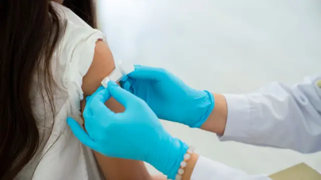 Doctor applies bandage to preteen girl's arm following an immunization.