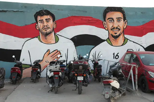 A massive public mural featuring detailed portraits of Iraq's national football team players