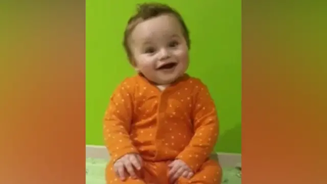 A small baby in an orange and white polka dot baby grow smiles