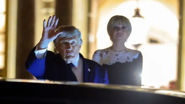 Donald Trump waves to reporters as he leaves Versailles, with Brigitte Macron behind him