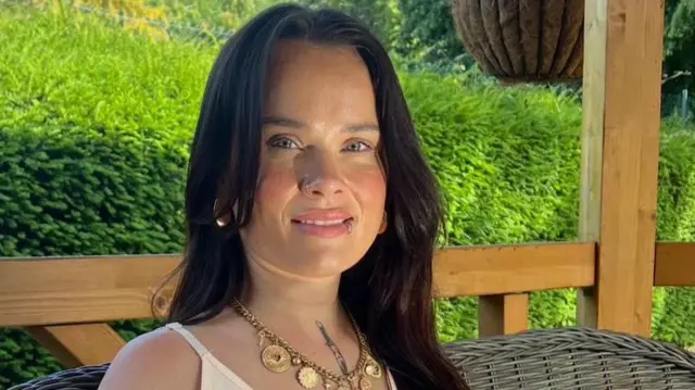 Natasha Hall smiling on holiday with a sunny green hedge behind her