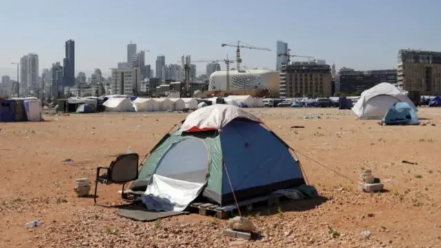 Lots of tents on a wide, flat space. In the background, there is a skyline of high-density buildings