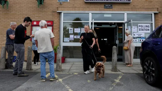 A woman, with her dog, leaves a polling station after voting in the Makerfield by-election
