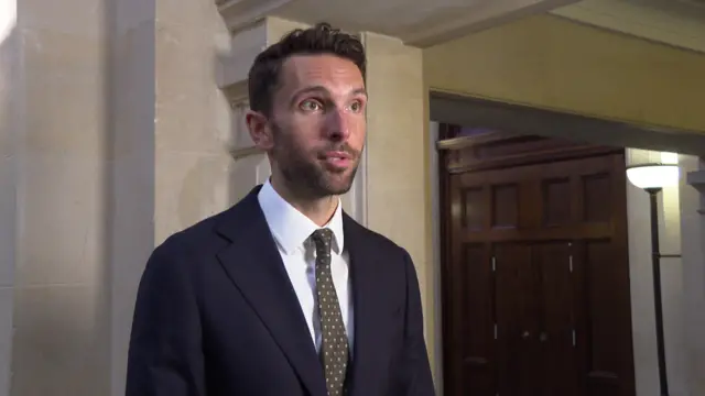 Josh MaCalister, with brown hair and wearing a suit and tie