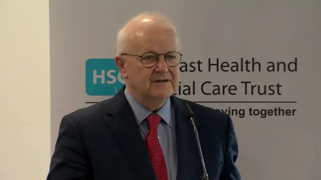 Elborn speaking. He is wearing a black suit, blue shirt and red tie.