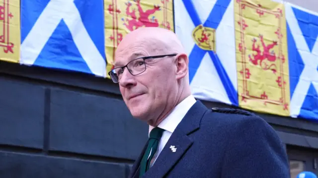 John Swinney walking in front of a row of Scotland flags