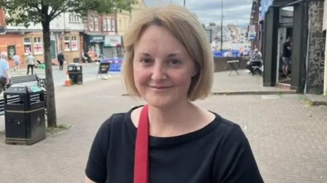 Gemma Crinigan, a blonde white lady in a black t-shirt stood in a high street.