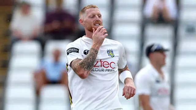 A grimacing Ben Stokes in cricket whites with his hand on his chin