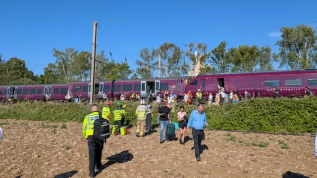 People are evacuated from two trains that have collided on a railway line. The emergency services help remove people from the trains.