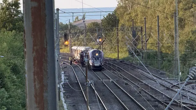 A train collision on a railway line during sunset. There are some uniformed workers and officers working near the trains.