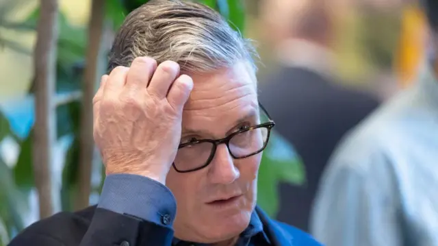 Prime Minister Sir Keir Starmer scratches his head as speaks with local residents