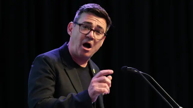 Andy Burnham stands at a podium mid-speech