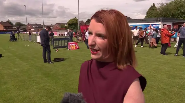 Louise Haigh speaks to media in a field. She is wearing a dark red dress.