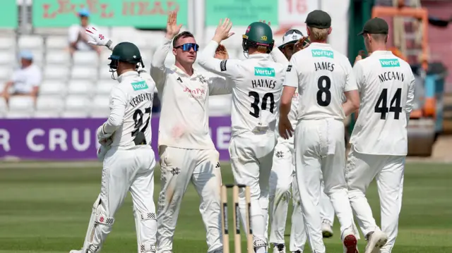 Liam Patterson-White wearing sunglasses is congratulated by team mates on taking the wicket of Charlie Bennett