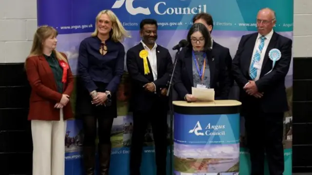 SNP candidate Lara Bird (second left) is announced as the winner of the Arbroath and Broughty Ferry by-election. She is stood on a stage smiling next to the other party candidates