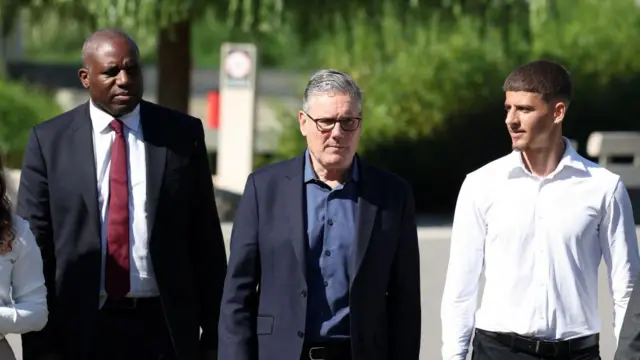 David Lammy and Keir Starmer walk outside with another man in a white shirt beside them.