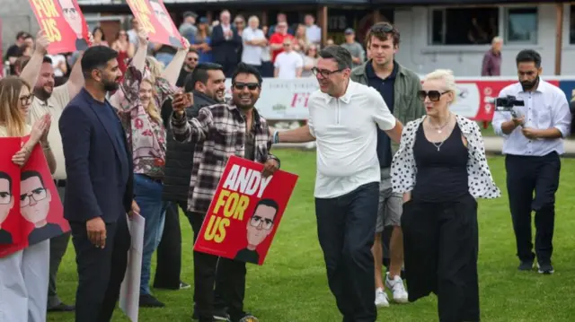 Outgoing Greater Manchester Mayor and newly elected Makerfield MP Andy Burnham walks with his wife past supporters holding signs reading 'Andy for us'