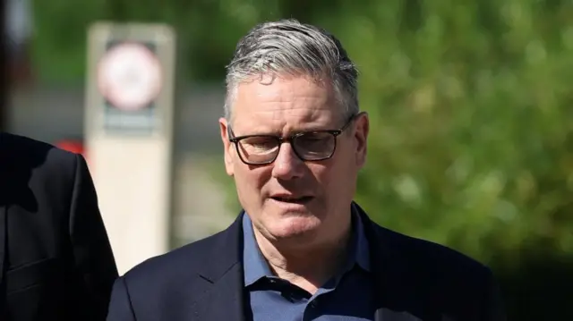 Keir Starmer walks outside wearing a dark-coloured suit jacket and navy shirt.