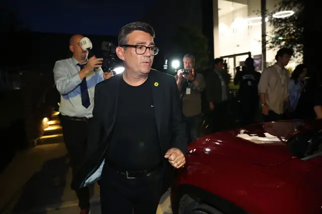 Burnham walks past his red car as papparazi take his photo from behind