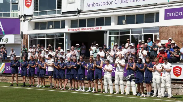 The players from Essex and Notts line up in front of the pavillion for a minutes applause in tribute to Paul Hiscock