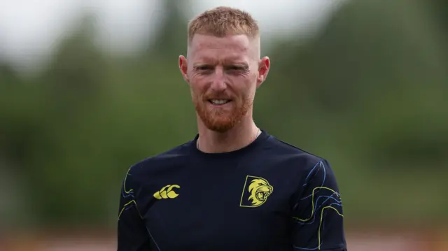 A smiling Ben Stokes looking at the camera wearing a dark blue Durham training top
