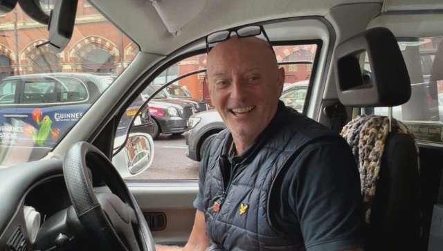 Bald, smiling cab driver with glasses on head